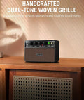 Compact 10W Guitar Amp With Clean And Drive Channel USB C Rechargeable Wireless Portable Practice Amp For Home And Travel Three Point Five Millimeter Headphone And Aux Jack Rich Analog Tone For Indoor Jams displayed on wooden table with woven grille design.