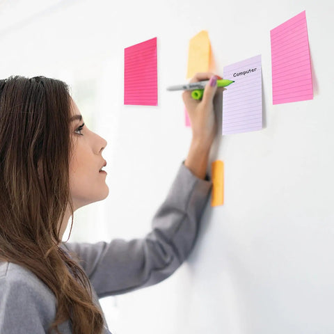 Person writing on pink 9 Pack 4x6 Lined Sticky Notes With Super Sticky Adhesive on wall, using memo pads for planning.