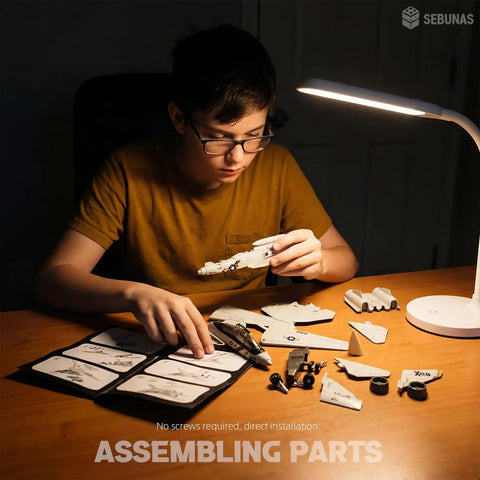 Person assembling F-14 Tomcat 3D Quick Build Model Kit For Adults Fighter Jet Puzzle with parts on desk under lamp.