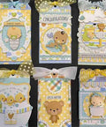 Handmade baby-themed scrapbook tags with cute animal designs, ribbons, and messages like 'Cute as a Button' and 'Congrats' on yellow and blue backgrounds.