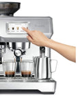 Heavy Duty Fully Automatic Espresso Machine With Slick Touchscreen Interface and Pro Grade Dual Boiler Rig For Killer Specialty Coffee At Home Featuring Precise Thermal Regulation And Smooth Simultaneous Brewing, hand selecting drink.