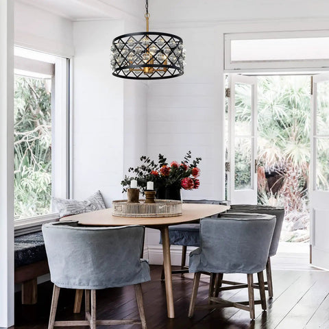 Dining area with elegant crystal chandelier in matte black and gold, above wooden table with gray chairs and floral centerpiece.