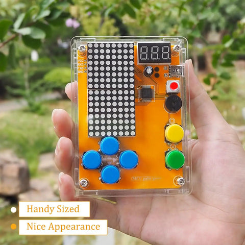 Hand holding the Hands On Solder Kit With Five Retro Game Classics For Electronics Practice And Learning Handheld Size In Clear Acrylic Case Easy To Build And Play Great Gift For Family And Friends, showing buttons and digital display in a garden.