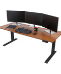 Heavy Duty Electric Standing Desk With Programmable Memory, Smooth Dual Motor Height Lift, Sturdy 3 Stage Telescoping Legs, Matte Black Frame And Warm Teak Surface, 72 Inch Flex Office Setup with dual monitors and keyboard.