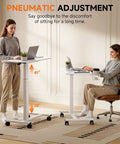Two women using Adjustable Pneumatic Standing Desk On Wheels With Lockable Casters Mobile Laptop Desk Overbed Bedside Table For Home Office 28 Inch Wide By 16 Inch Deep White, showing height range.