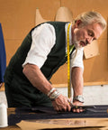Tailor measuring fabric on a table in a workshop with sewing patterns on the wall.