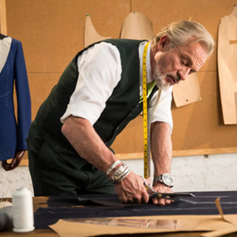 Tailor measuring fabric on a table in a workshop with sewing patterns on the wall.