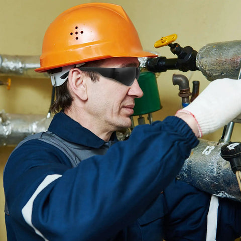 Man wearing Bulk 100 Safety Glasses Set For Men And Women Eye Protection Goggles With Scratch Resistant And Impact Resistant Lenses Ideal For Work Construction Lab Science Outdoors Dark Black while working with pipes.