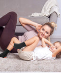 Mother and child exercising on carpet with Youth Ankle Compression Sleeve For Active Kids Knit Ankle Brace visible on child's ankle.
