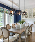 Dining room with three Farmhouse Black Globe Cage Pendant Light fixtures over wooden table, chairs nearby.