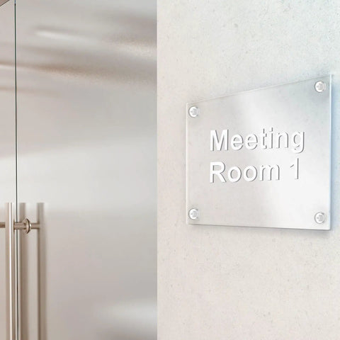 Clear acrylic meeting room sign with screws on wall showcasing "Meeting Room 1" text.