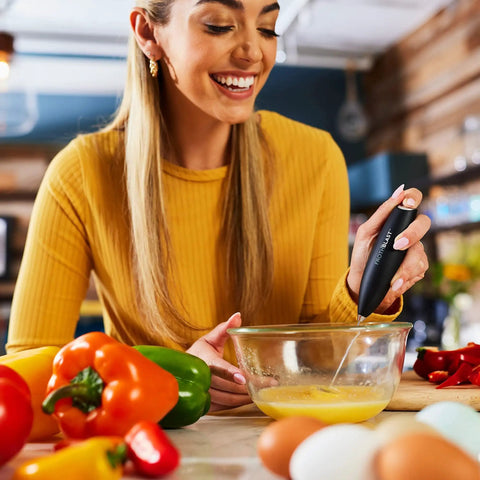 Woman using Powerful Handheld Milk Frother For Coffee Lovers, Quick Foam Maker Whisk beside fresh vegetables in kitchen.