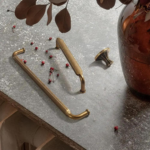 Antique Brass Zinc Alloy Cabinet Pulls 12 Pack Three And Three Quarters Inch Hole Centers Drawer Handles for Kitchen Cabinets and Dressers Vintage Vibe Durable Boss Grade Hardware on stone surface with vase