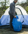 Person using Blue Camping Stuff Sack With Water Resistant Polyester For Sleeping Bags And Gear, 18 By 30 Inch, near tent