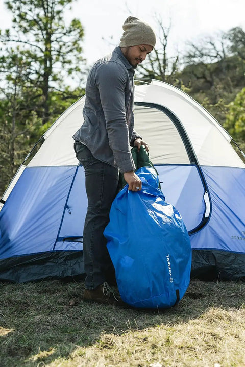Person using Blue Camping Stuff Sack With Water Resistant Polyester For Sleeping Bags And Gear, 18 By 30 Inch, near tent
