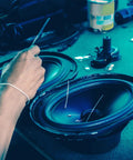 Person repairing speaker with wires on table, tools scattered, blue tint lighting