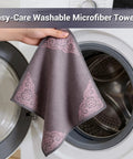 Microfiber cleaning cloth, gray with pink corner floral pattern, hand-held beside a front-loading washing machine.
