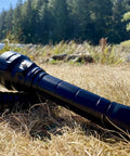 Beast 5000 Lumen DL40 Diving Flashlight with LH351D LEDs lying on grass near a lakeside, showing rugged design for outdoor use.