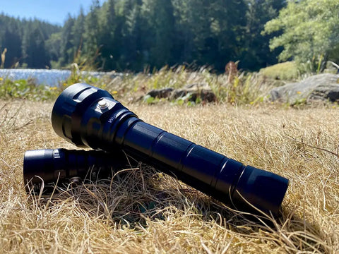 Beast 5000 Lumen DL40 Diving Flashlight with LH351D LEDs lying on grass near a lakeside, showing rugged design for outdoor use.