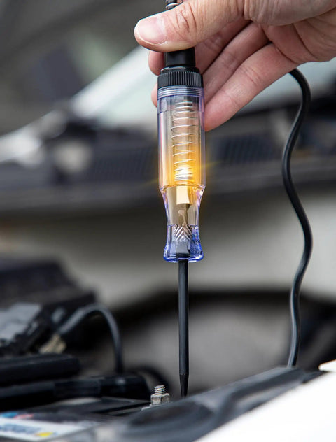 6V-12V-24V DC Car Electrical Test Pen With Alligator Clip And Long Steel Probe, Continuity And Voltage Fuse Tester For Sedan, SUV, RV And Truck, Handy Automotive Test Light For Quick Circuit Checks. Hand holding lit probe on car battery terminal.