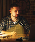 Rechargeable 12 LED Warm Clip On Book Light With Dual Goosenecks Bed Reading Lamp in use by man at desk with laptop and book.