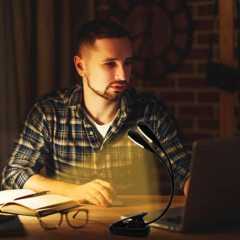 Rechargeable 12 LED Warm Clip On Book Light With Dual Goosenecks Bed Reading Lamp in use by man at desk with laptop and book.