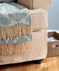 Beige armchair with decorative blue and beige fringed throw blanket, positioned on hardwood floor near woven basket.