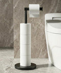 Freestanding Toilet Paper Holder Stand With Extra Heavy Weighted Base And Non Slip Mat Sleek Black Modern Bath Decor next to a toilet.