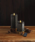 Hexagon Flameless Moving Flame Pillar Candles Set Of 2 in chalky black finish on wooden table with remote and fall decor.