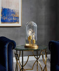 Vintage Brass Glass Cloche End Table Lamp With Industrial Modern Vibe on round glass table between blue armchairs