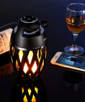 LED Flame Outdoor Table Lamp With Bluetooth Speaker Rechargeable Ambience Lantern With Flickering Warm Light beside wine and phone.