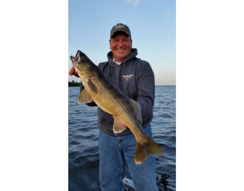 Angler holding a large fish by a lake, using Budget Friendly Monarch Spinning Rod And Reel Combo 5 Foot 6 Inch, 2 Piece Graphite Rod.