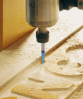 Engraving router bit with blue-coated carbide tip installed in CNC spindle, cutting a 30-degree V-groove in wood.