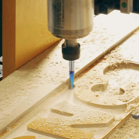Engraving router bit with blue-coated carbide tip installed in CNC spindle, cutting a 30-degree V-groove in wood.