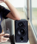 R1850DB Dope Active Bookshelf Speakers with Bluetooth and Optical Input next to person holding wine glass