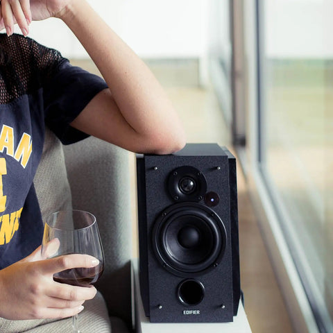 R1850DB Dope Active Bookshelf Speakers with Bluetooth and Optical Input next to person holding wine glass