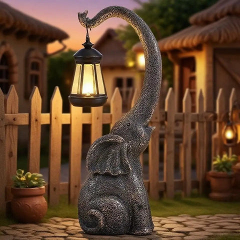 Outdoor Solar Powered Elephant Garden Statue With LED Lantern Lights sits on a patio, featuring a trunk lantern, cozy night glow.