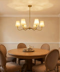 Smooth Operator 6 Light Brass Gold Chandelier With White Fabric Shades above round dining table in cozy setting.