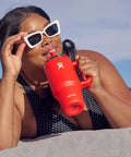 On The Fly 40 Oz Stainless Steel Travel Tumbler With Comfort Grip Handle And Leak Proof Straw Lid used at beach, woman sipping drink.