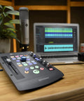 IoStation 24C 2x2 USB Audio Interface and Production Controller on desk with laptop and microphone, featuring 100mm motorized fader.