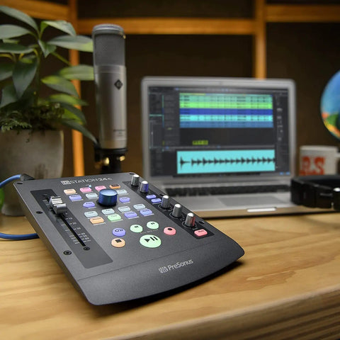 IoStation 24C 2x2 USB Audio Interface and Production Controller on desk with laptop and microphone, featuring 100mm motorized fader.