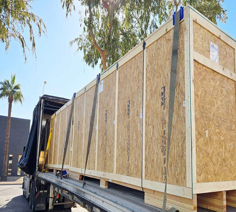 Large wooden crates secured with straps on a flatbed truck, using 20 Pack 4 Inch Edge Protectors For Flatbed Trucks With Mesh Carrying Case.