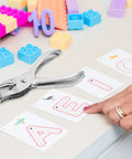 Dope 20 Pack One Quarter Inch Single Hole Punch Set, Metal Hand Paper Puncher on a desk with alphabet cards and colorful blocks