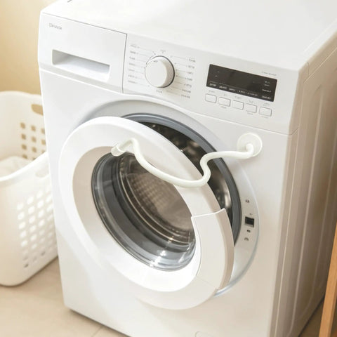 Magnetic Front Load Washer Door Prop And Dryer Vent Holder With Grippy Silicone Base To Keep Your Machines Cracking Open And Smelling Totally Fresh White attached to a washing machine.