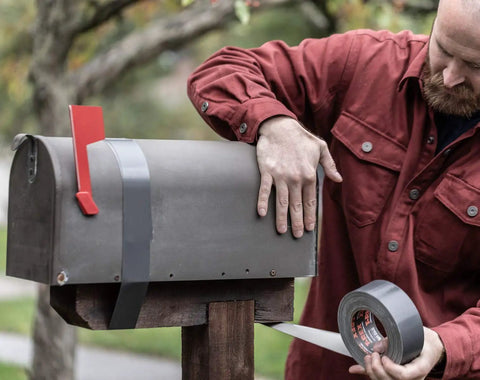 Applying Ferociously Strong Duct Tape 105 Yards Triple Pack Gunmetal Gray to fix metal mailbox outdoors, showing premium adhesive.