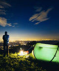 Ultra Bright 1500 Lumen Rechargeable Tactical Flashlight illuminating a campsite with a tent and person, city lights in background