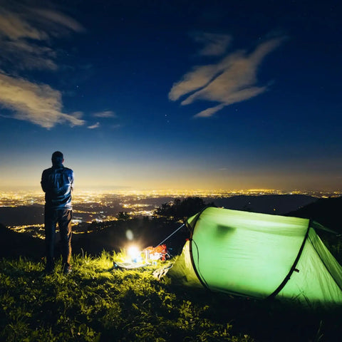 Ultra Bright 1500 Lumen Rechargeable Tactical Flashlight illuminating a campsite with a tent and person, city lights in background