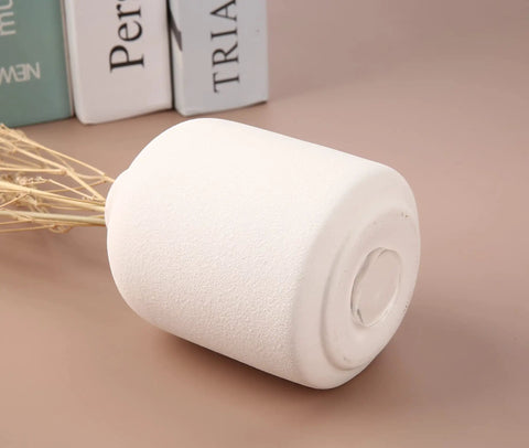 Minimalist white ceramic vase with simple round design on a brown surface, next to a stack of books and dried branches.