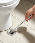 Flexible Drain Snake Cleaner Brush That Kicks Out Greasy Gunk Reusable Spiral Hair Removal Tool With Comfort Grip Handles For Sinks Showers And Bathtubs In White in use on a bathroom floor drain.