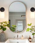 Farmhouse Style 2 Light Wall Vanity Light Fixture With Glass Shades in bathroom with mirror above sink, matte black metal
